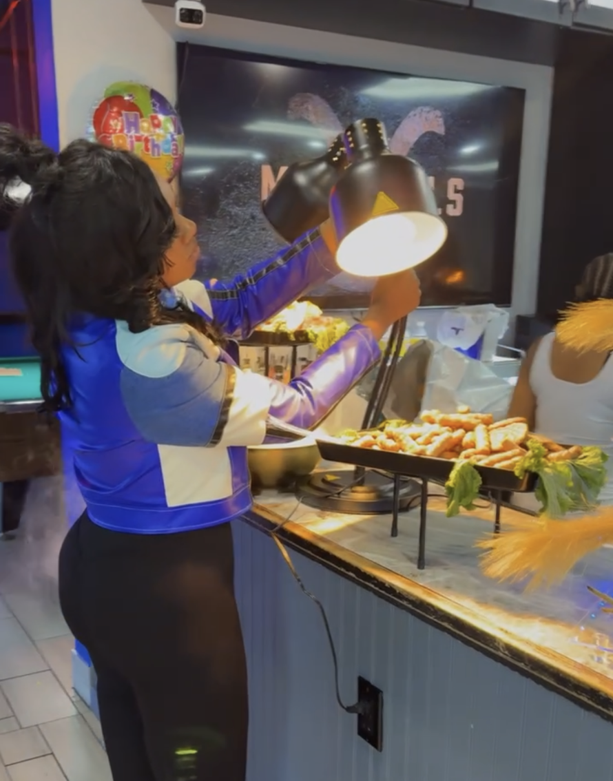 Chef Nesha adjusting a heat lamp over a hot food display